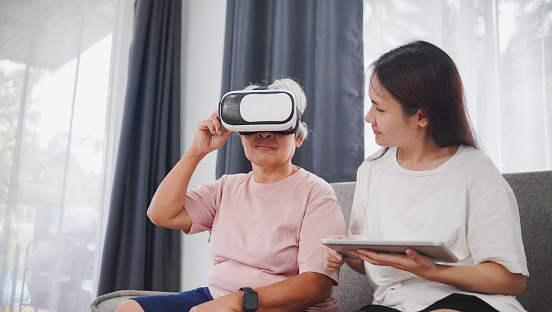 Concept Virtual Reality Technology, Asian woman is powering image signal from tablet to 3D VR glasses that Asian elderly woman is wearing.