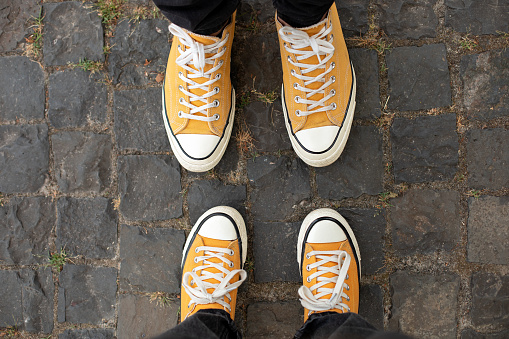Close Up Feet of man and woman in stylish casual shoes. Male and female in yellow sneakers being walking down the street. Man and woman Legs In in shoes Walking on sidewalk.