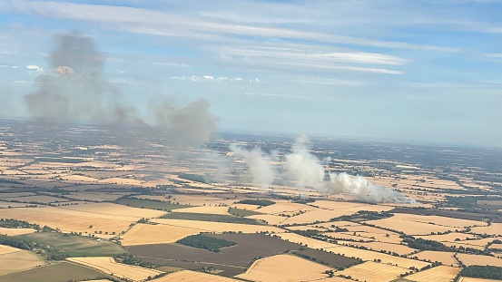 Farming field on fire during extreme heatwave in Hertfordshire with long smoke trail
