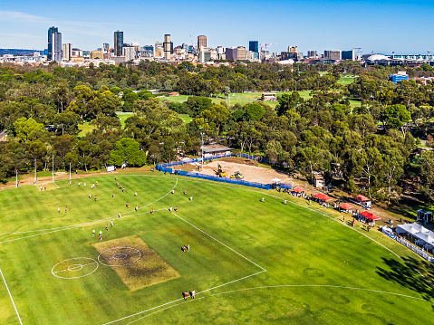 Adelaide, Australia - June 18, 2022: Aerial view Adelaide parklands football field in Bundey's Paddock (Tidlangga Park 9) with city skyline background. Amateur game in progress of Australian Rules Football on public property game, play is concentrated in one area of the playing field. Spectators are sitting under portable shelters. Public park (open green space) with some construction/renovation taking place.\nRe-submitted: refer Contributor Services Ticket CS0507715