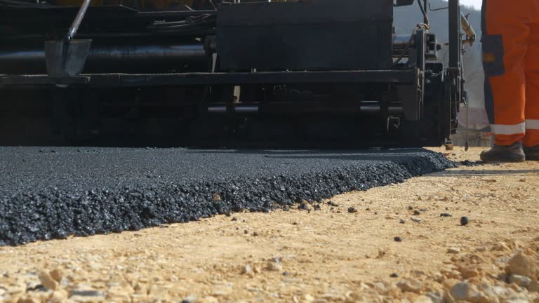 CLOSE UP: View from back of paver machinery leaving behind freshly laid asphalt