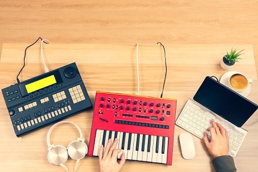 top view of professional music producer, composer hands arranging music on computer and recording equipments on desk. music production technology, home studio