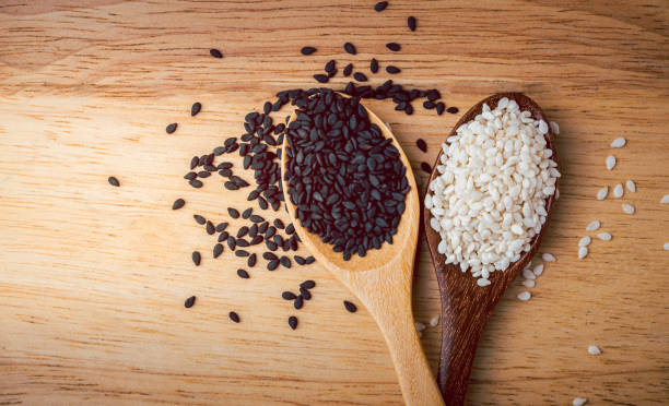 semillas de sésamo blancas y negras en una cuchara de madera en el fondo es una mesa de madera, concepto de alimento orgánico. - sesame black stack cereal plant fotografías e imágenes de stock