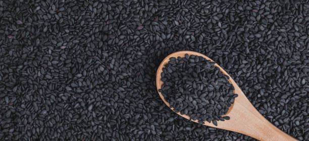 zbliżenie czarnych nasion sezamu w drewnianej łyżce na czarnym sezamie tło makro shot, koncepcja żywności ekologicznej. - sesame black stack cereal plant zdjęcia i obrazy z banku zdjęć