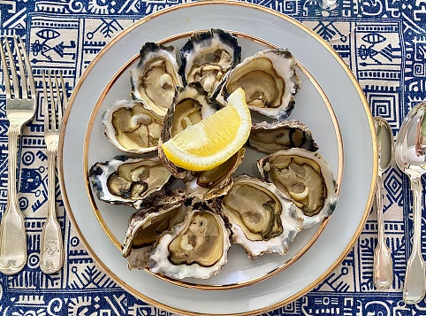Horizontal flat lay of fresh shucked local Australian oysters with lemon on white and gold porcelain plates ready to eat with crisp white wine on blue and white placemat for Christmas entree