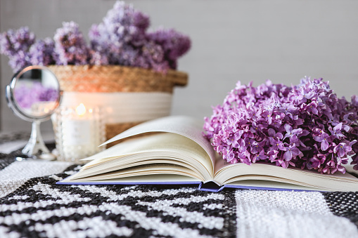 Wicker basket with lilacs, a candle, an open book on the table.Good morning concept.