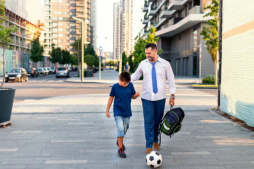 Photo of a happy father returning home from school with his son. They walking  in the city streets and having a lot of fun.