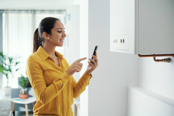 휴대 전화를 사용하여 스마트 보일러를 관리하는 여성 - heating engineer 뉴스 사진 이미지