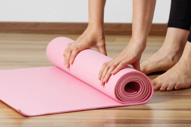 Woman rolling exercise mat in living room.