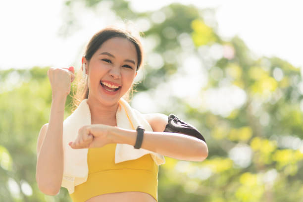 cheering asian smile female sport woman athlete on a morning run rejoices victory,female checking time on his wrist watch in fitness clothes say yes for jogging running beat the score hersellf workout stock photo