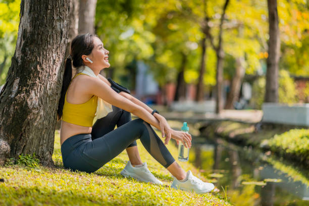 détendez-vous femme sportive asiatique décontractée temps de pause après la fin de la course du matin exercice mode de vie sain, femme asiatique détendez-vous se rafraîchir après l’entraînement de course sous l’arbre près de l’eau dans le pa - running jogging asian ethnicity women photos et images de collection