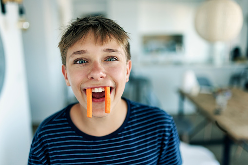 Teenage boy eating carrots. The boy is making funny face pretending to be a healthy carrot vampire.
Shot with Canon R5