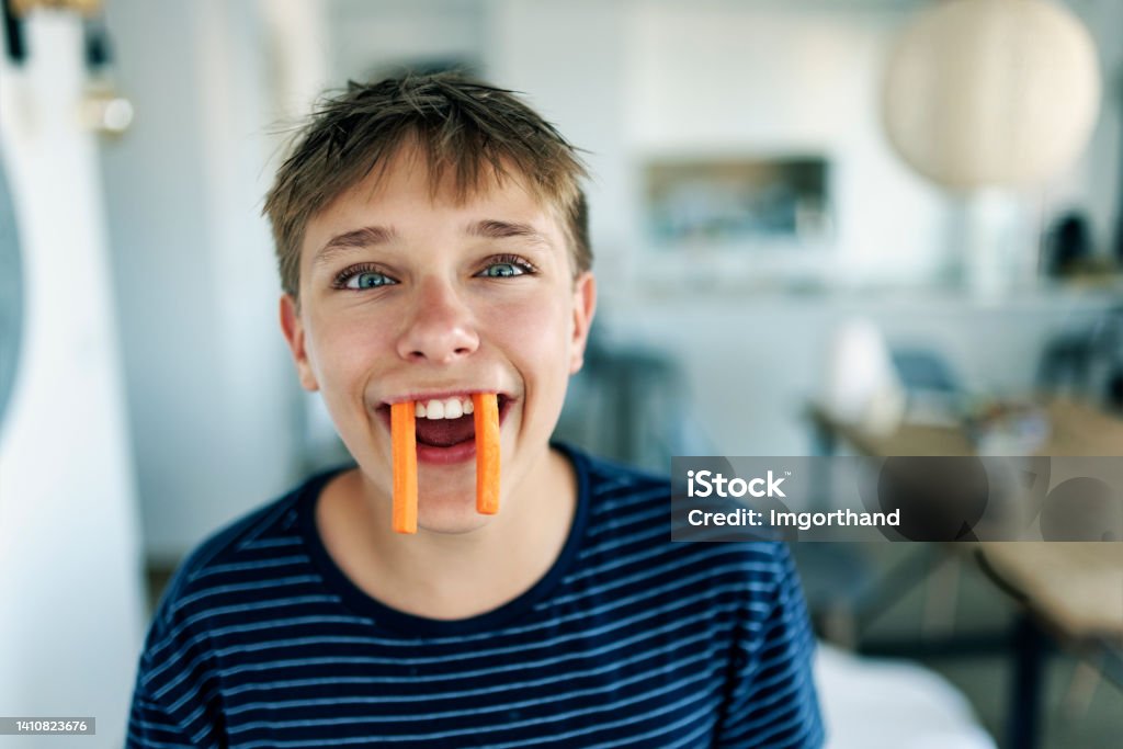 Portrait of a carrot vampire Teenage boy eating carrots. The boy is making funny face pretending to be a healthy carrot vampire.
Shot with Canon R5 Humor Stock Photo