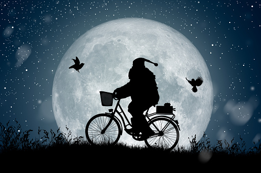 Silhouette of Santa Claus riding on his bicycle to carry a gift under the Milky Way background and full moon.