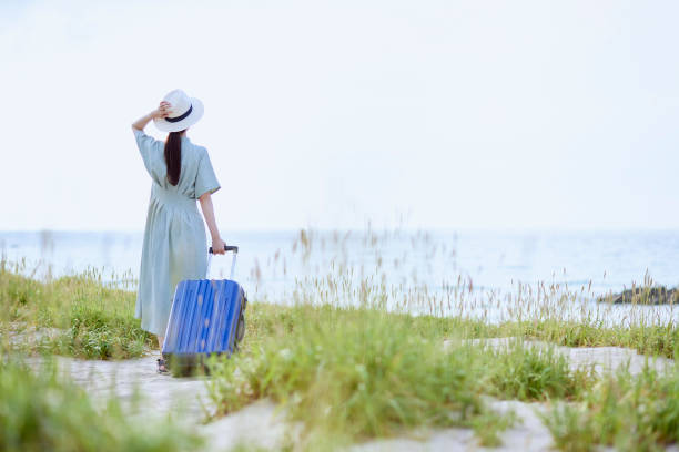 スーツケースを持って浜辺に立つ日本人女性