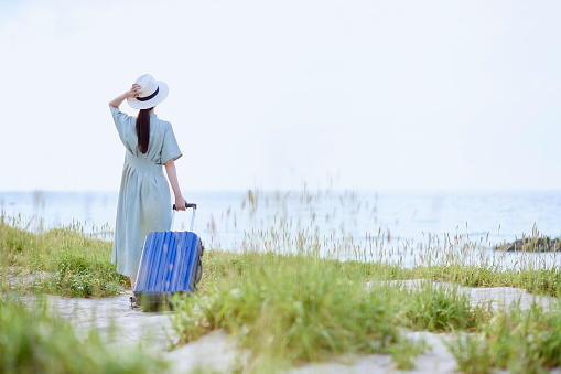 Japanese woman standing on the beach with a suitcase