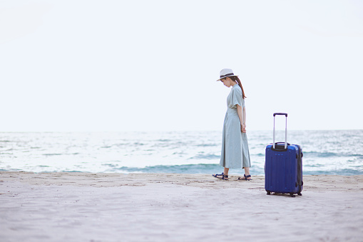 Japanese woman standing on the beach with a suitcase