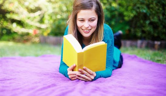 Attractive woman in her early 20s reading a book as she lies in an idyllic garden.