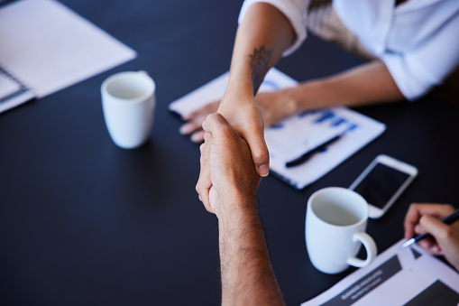 Close-up of two businesspeople shaking hands across a conference table during a boardroom meeting in an office