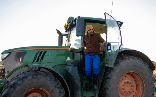 Allow angle wide view of a young trainee farmer exiting a tractor he is learning to drive in a farm in Northumberland in the North East of England.