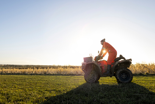A side view of a male farmer on his quad bike on a bright morning on the farm he works at in Northumberland in the North East of England.