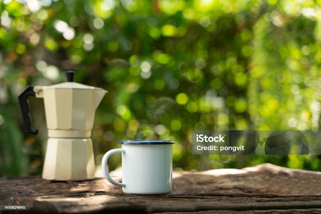 Hot coffee in a white enamel mug on an old wooden floor while camping in the forest. soft focus.shallow focus effect. Camping Stock Photo