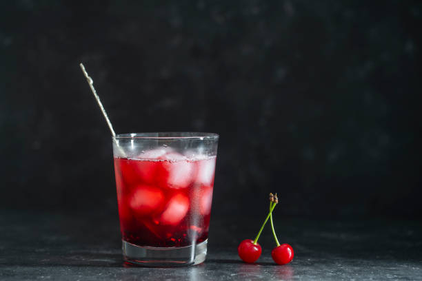 Fresh red cherry cocktail with ice cubes in glass on black background. Summer iced refreshing drink stock photo