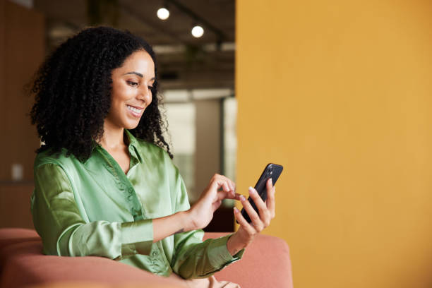 Smiling young businesswoman using her phone in an office lounge stock photo