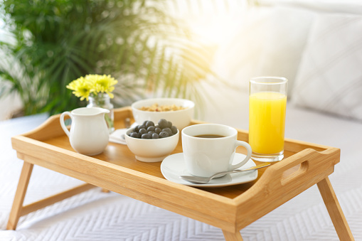 Wooden tray with breakfast on the bed in a hotel room, romantic morning with healthy food