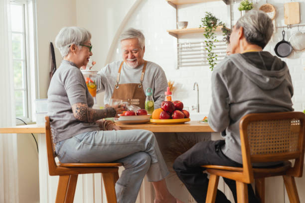 gruppe von älteren freunden, die drinnen feiern, kochen und positive gespräche in der seniorentagesstätte führen, asiatische ältere männer, die in der küche stehen und sich zu hause entspannen, während sie ein gesundes essensrezept essen - two parent family indoors home interior domestic kitchen stock-fotos und bilder