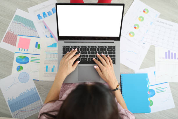 istock Freelancer using laptop next to papers with charts sitting on floor top view 1410834462
