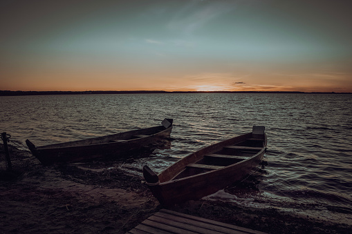 Two wooden boats are moored near the lake at sunset time