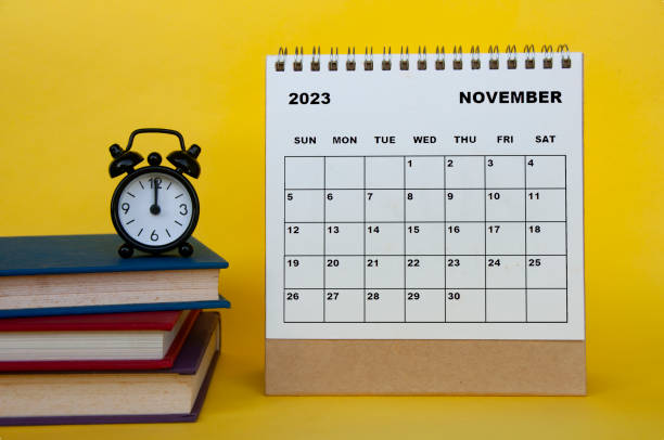 2023年11月の机のカレンダー、黄色の背景に本と目覚まし時計。