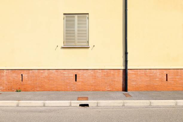 Metallic window shutter on a red and yellow facade. Concrete sidewalk and asphalt road in front.