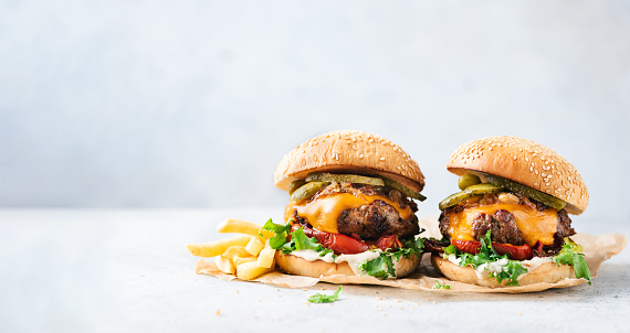 Two craft cheeseburgers and fries on parchment paper over grey concrete background. Copy space. Web banner burgers