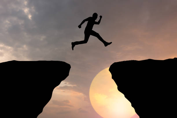 istock Silhouette young man jumping over precipice between two rocky mountains at sunset. 1410839692