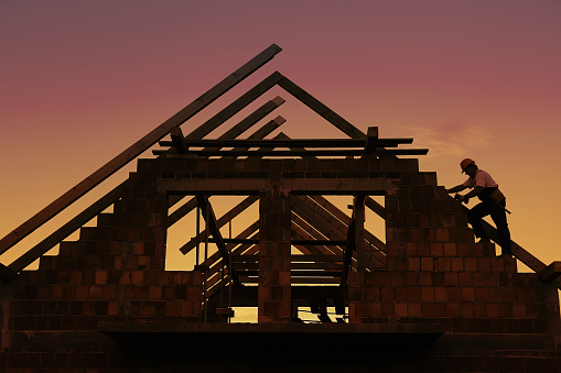 Construction worker working with house wooden roof against sunset sky