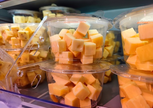 Plastic container with cubes of cheese in it is being sold without visible marks or brands on a supermarket shelf. There are no people or trademarks in the shot.