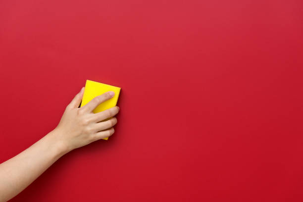 Cleaning concept. A hand in a yellow glove squeezes a yellow cleaning sponge with a hard side