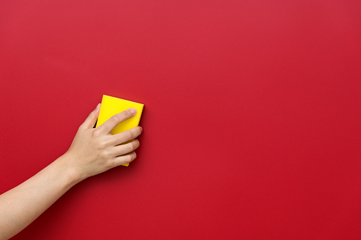 Woman hand cleaning red wall with sponge.