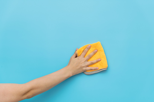 Woman hand cleaning blue wall with rag.