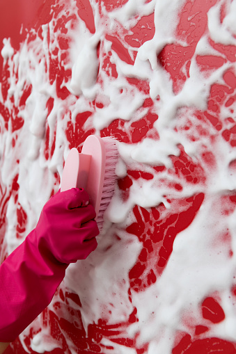 Woman hand cleaning blue wall with brush.