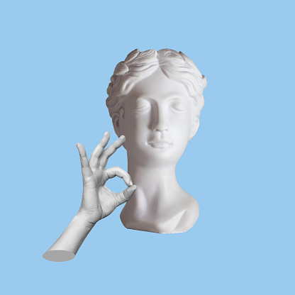 Antique female statue's head shows the ok gesture with hand isolated on a blue color background. Trendy abstact collage in magazine surreal style. 3d contemporary art. Modern design