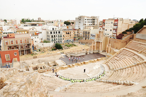 15th June, 2022. Group of students sat in an ancient amphitheater in Cartagena, Spain, listening to a local guide