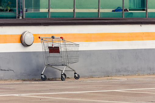 Dumped shopping cart in a parking lot outside mall. Abandoned handcart next to a building