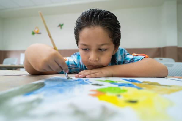 A little latin boy painting with a paintbrush in class and looking closely.