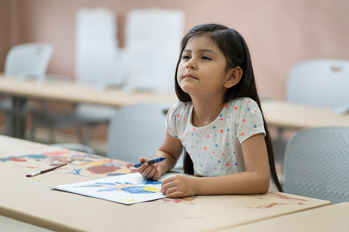 A little latin girl sitting in class and squinting to see the board.