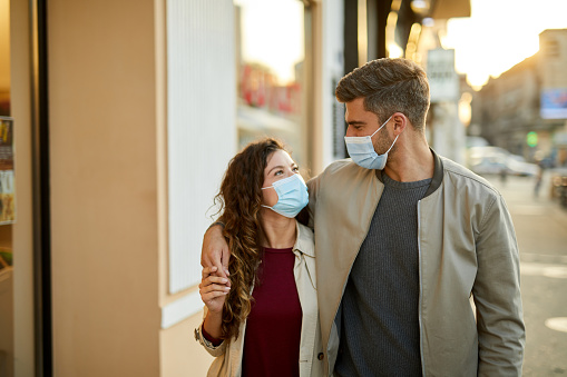 Mid adult couple with protective masks walking down the street together during the coronavirus epidemic