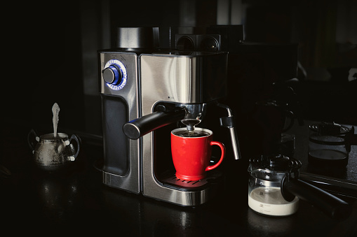 coffee maker and mug and milk on a black dark background . making coffee at home