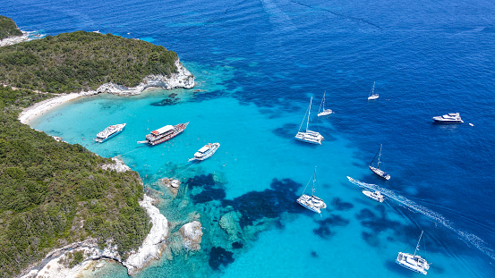 Aerial drone photo of sail boats anchored in tropical Caribbean island paradise bay with white rock caves and turquoise clear sea. Beach with deep turquoise sea visited by sail boats